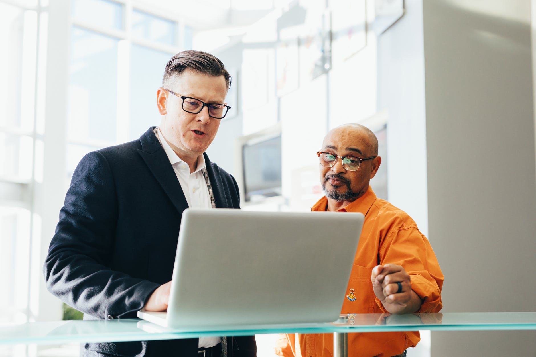 Two men stand at a computer discussing how to get technical support from briskData